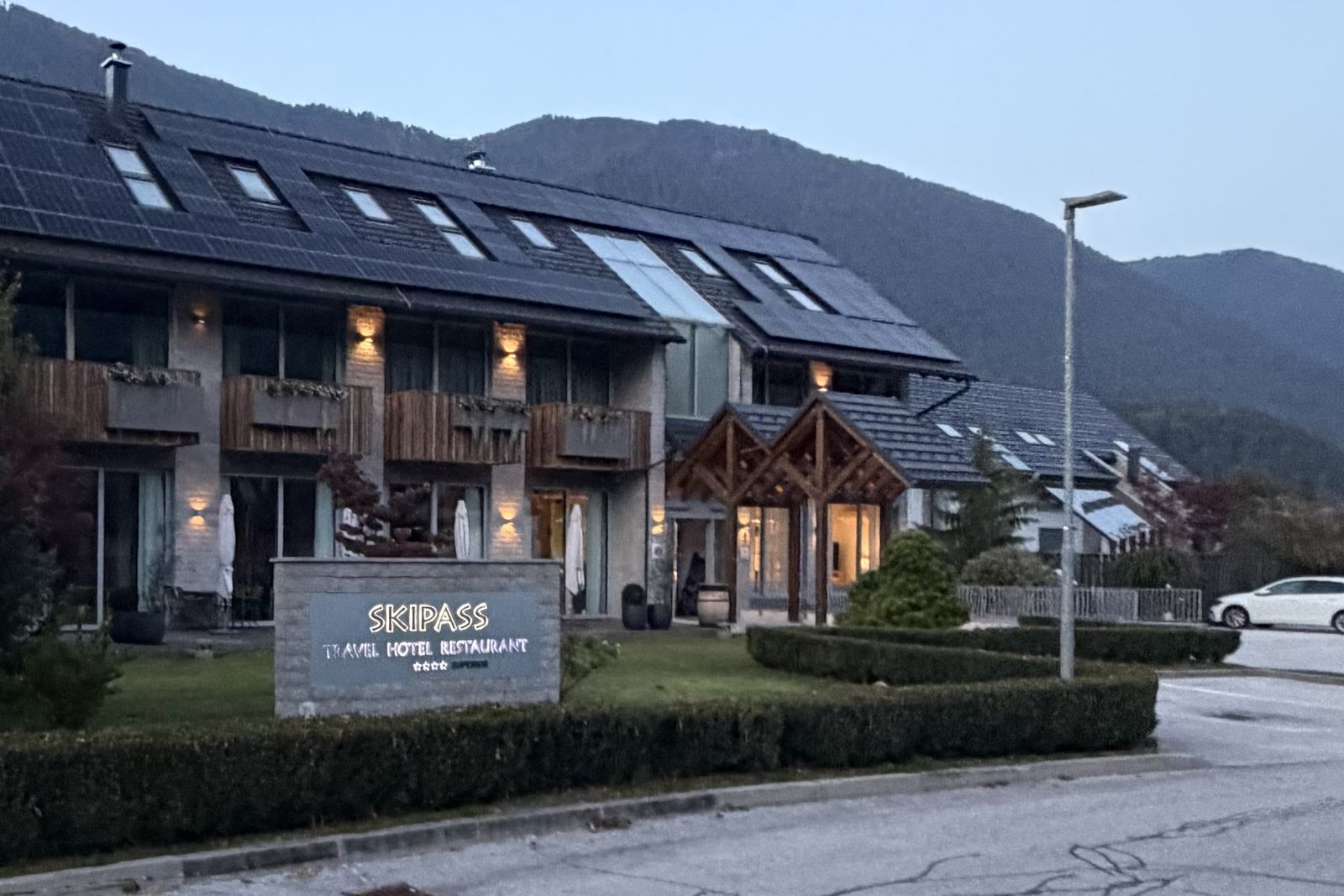 Boutique Hotel Skipass at dusk, with its lit sign and the mountains behind