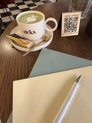 Matcha latte in a Neks cup next to letter-writing paper and pen